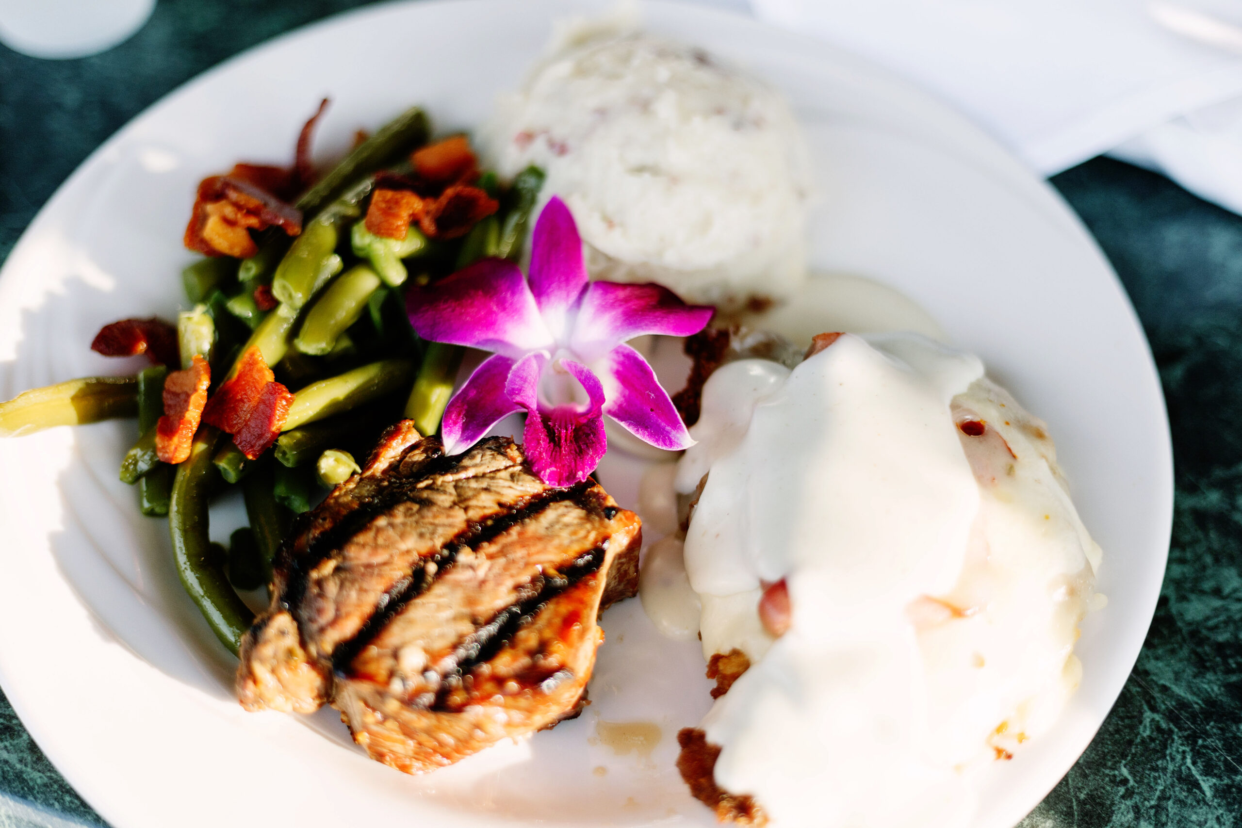 Elegant plated wedding dinner featuring grilled meat, green beans, potatoes, and an orchid garnish by Ceruti’s Catering in Fort Wayne.
